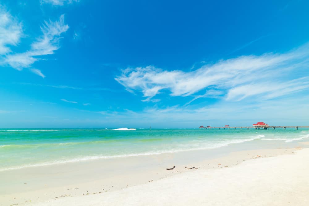 An expanse of white sand leading to the turquoise water of Clearwater Beach with a pier in the distance.