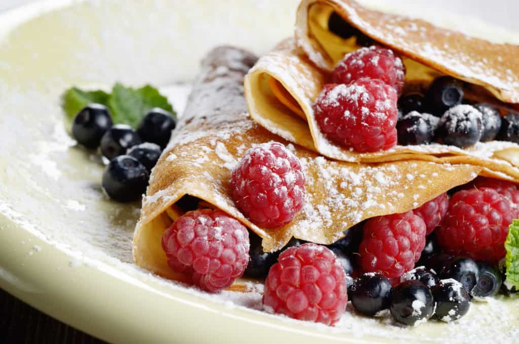 Delicious sweet crêpes with fresh raspberries and blueberries covered with powdered sugar