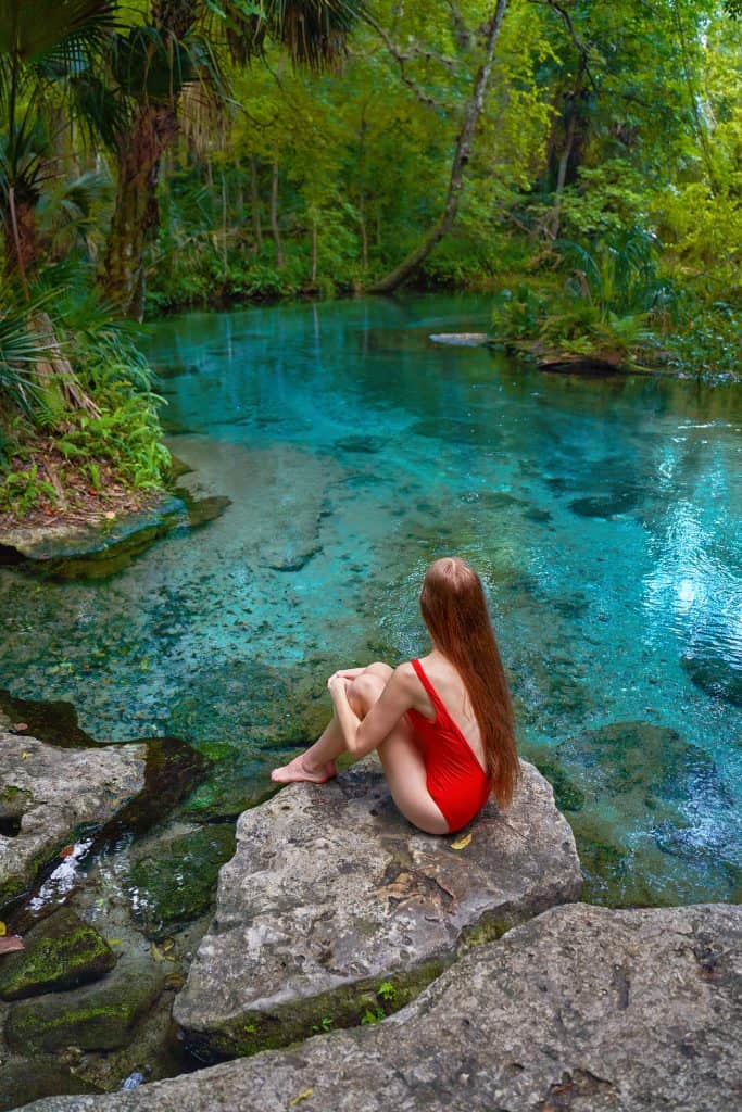 woman in red bathing suit sitting on a rock with blue water in the background at rock springs