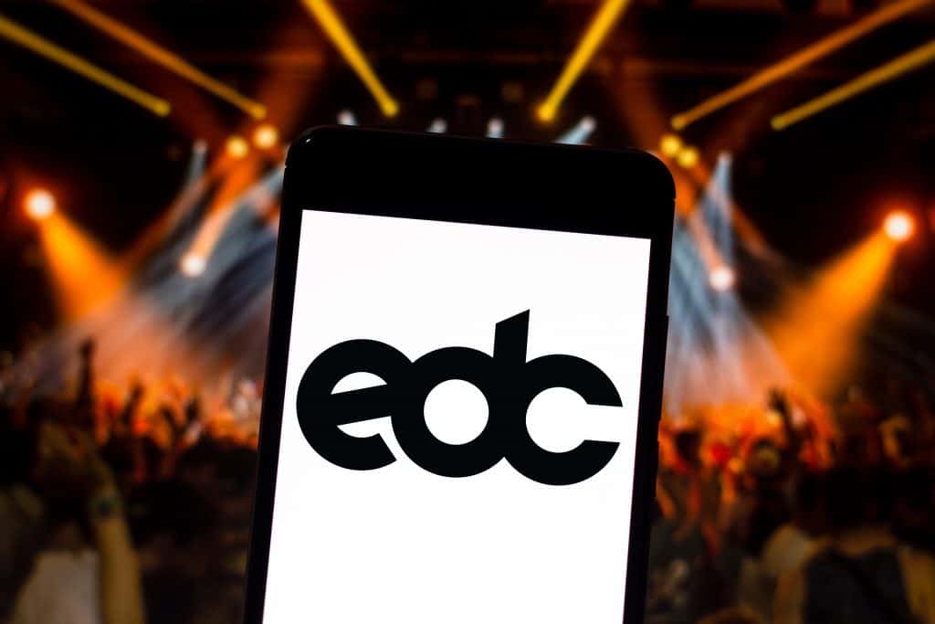 The logo of the Electric Daisy Carnival displayed on a cell phone, floating over a sea of concert-goers at one of the biggest and brightest fairs in Florida.