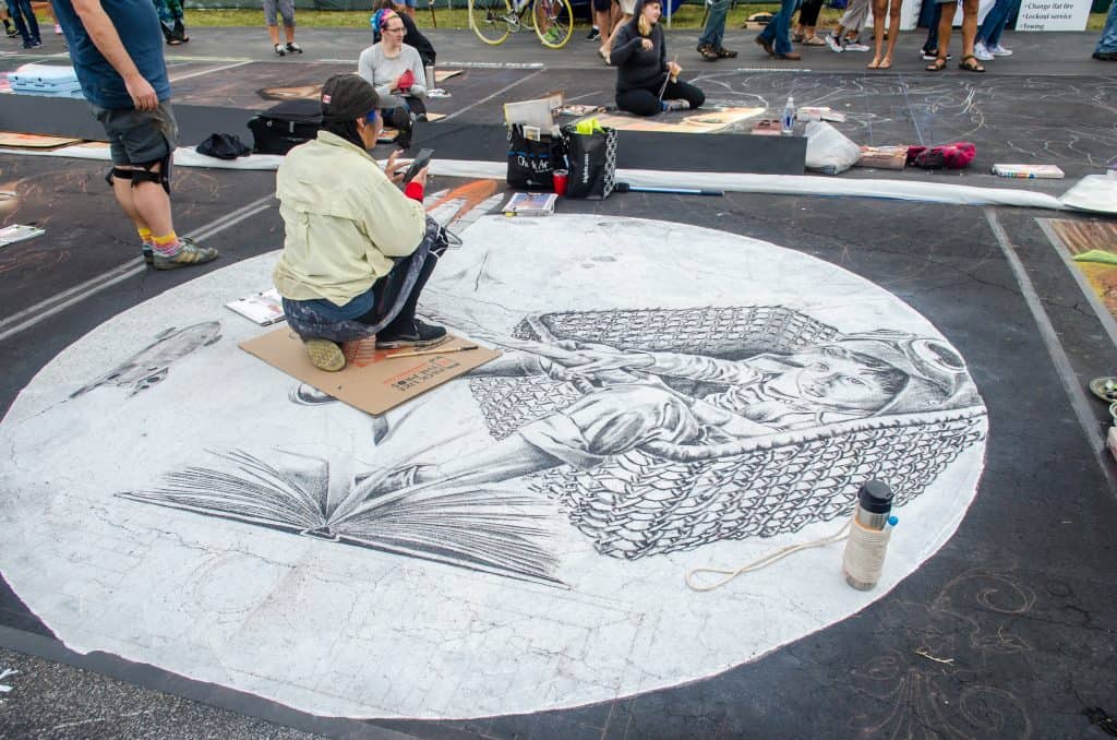 An artists works on a massive chalk masterpiece of a boy in a basket at the International Chalk Festival in Venice Beach, Florida.