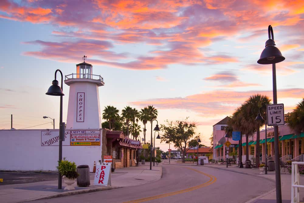 Tarpon springs is one of the small beach towns in Florida home to Greek population with a lighthouse in foreground and shops in background during sunset