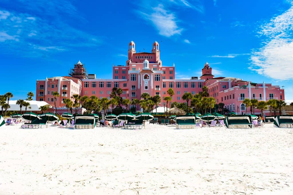 The large pink palace of Don CeSar Hotel sitting right on the beach, with palm trees and beach umbrellas, one of the best places to visit in St. Petersburg if looking to relax.