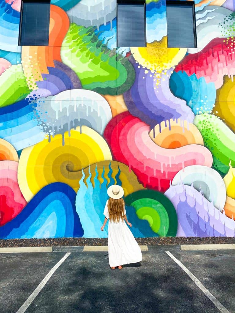 A woman with long hair and dress stands looking at a bright-colored mural located in downtown St. Petersburg Florida in the central arts district.
