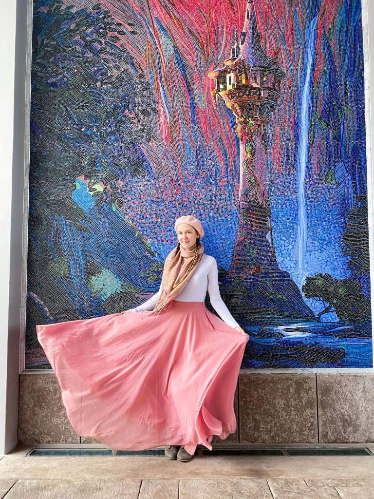 Victoria poses in front of a Tangled mosaic at Disney World dressed for warmth in Florida in the winter.