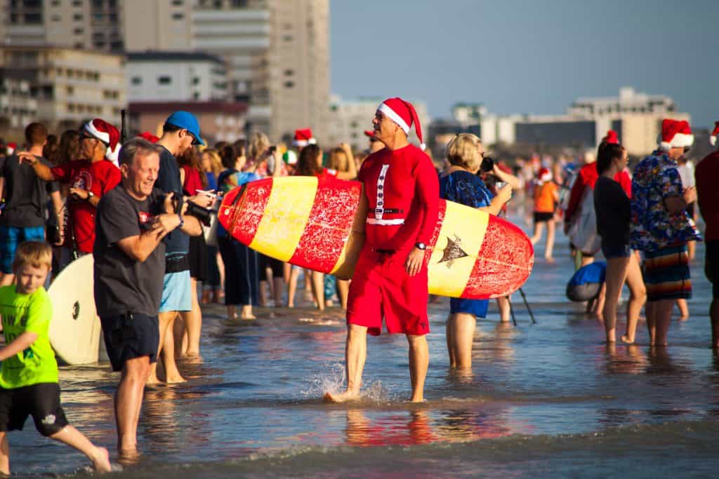 A surfer dressed as Santa walks along Cocoa Beach during Surfing Santas