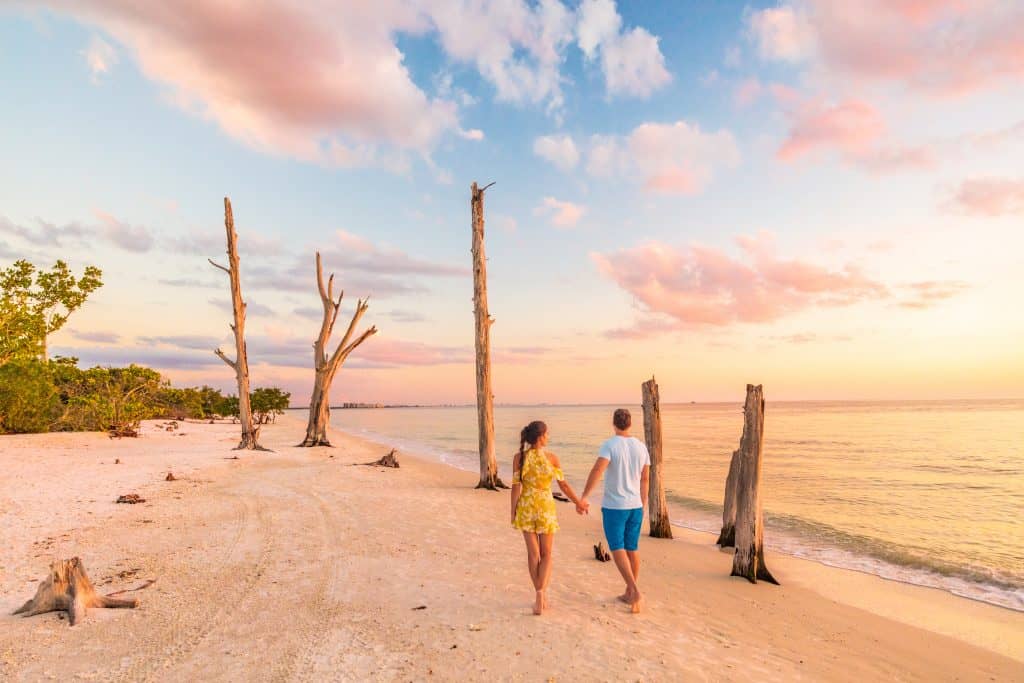 A couple walks hand-in-hand away from the camera, along a beach at sunset on a romantic getaway in Florida.
