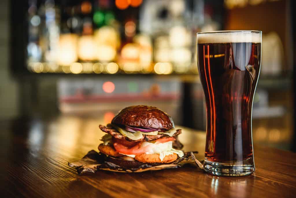 Photo of a dark beer and sandwich in a pub setting. 