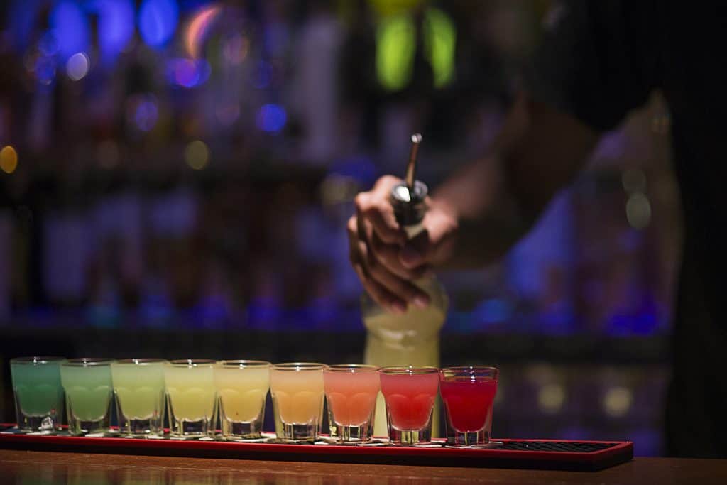Photo of rainbow colored shots lined up on a bar top.