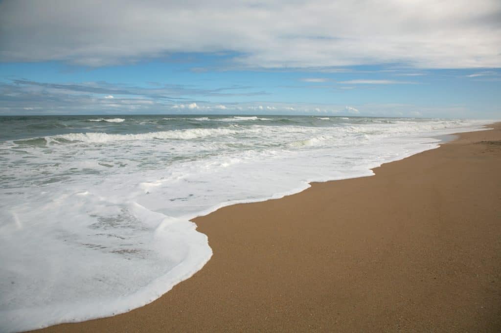 The dark brown sands of Apollo Beach lie under beautiful waves.
