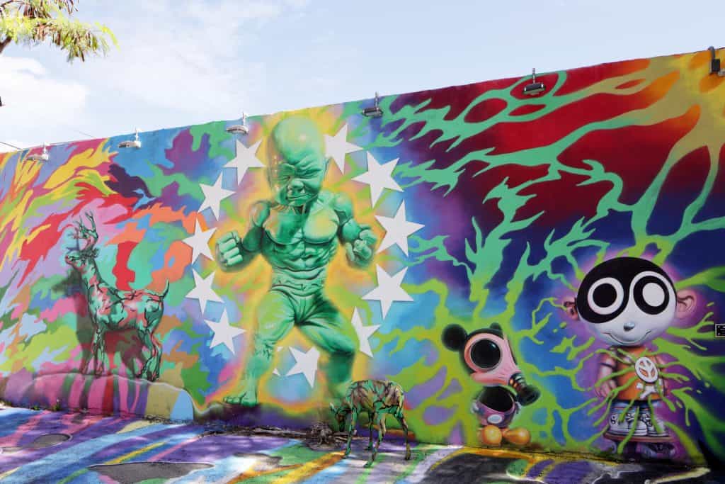 A mural features a green baby with muscles and Mickey Mouse wearing a gas mask.