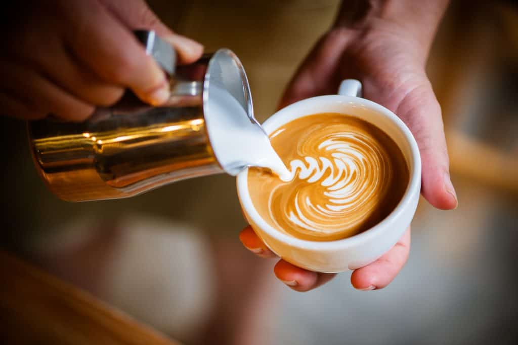 A barista pours velvety microfoam into rosetta design over espresso.