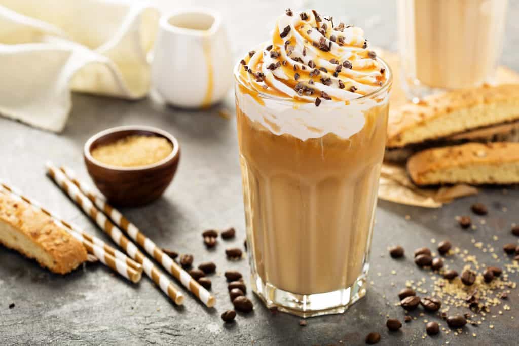 An iced coffee is topped with whipped cream, caramel and chocolate chips.