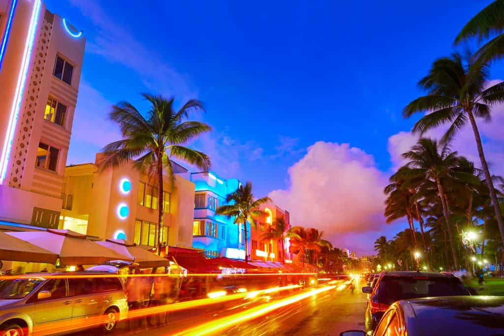 Cars rush down a street lined by colorful buildings in Miami Beach, one of the best day trips from Naples.