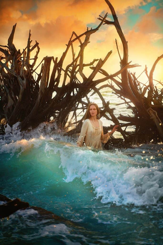 Victoria wades through the waves in front of driftwood at Beer Can Island, one of the best things to do in Siesta Key.