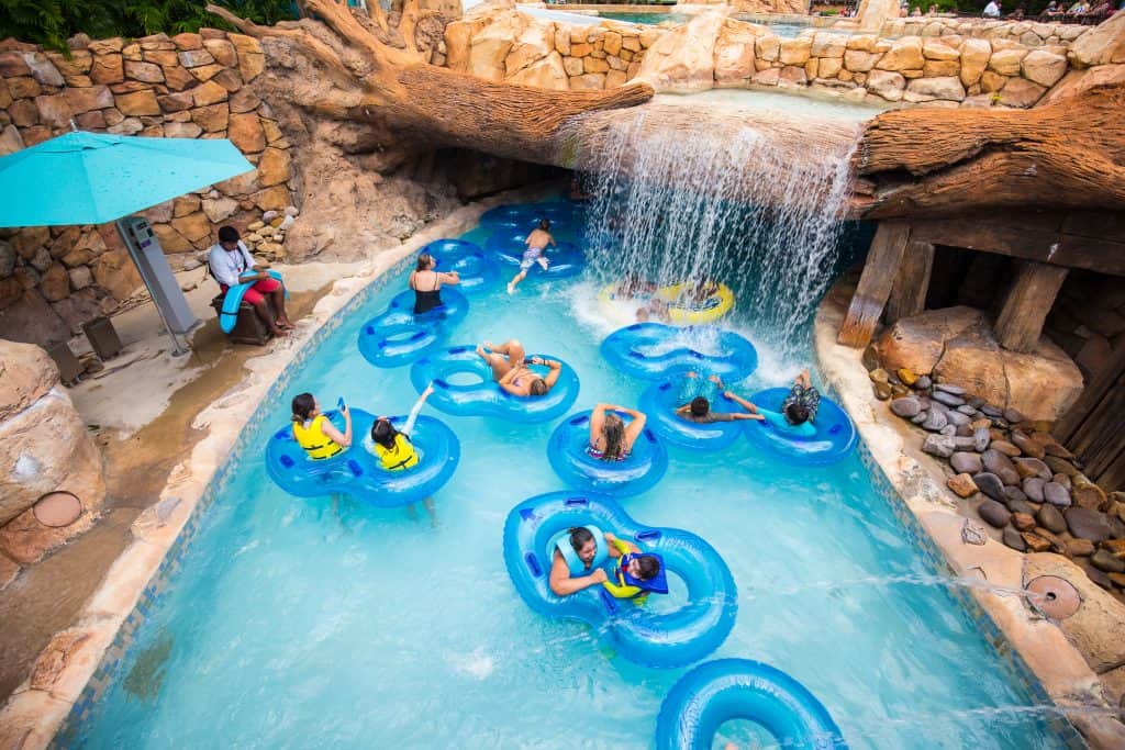 People in inflatable tubes wading under a waterfall through a lazy river.