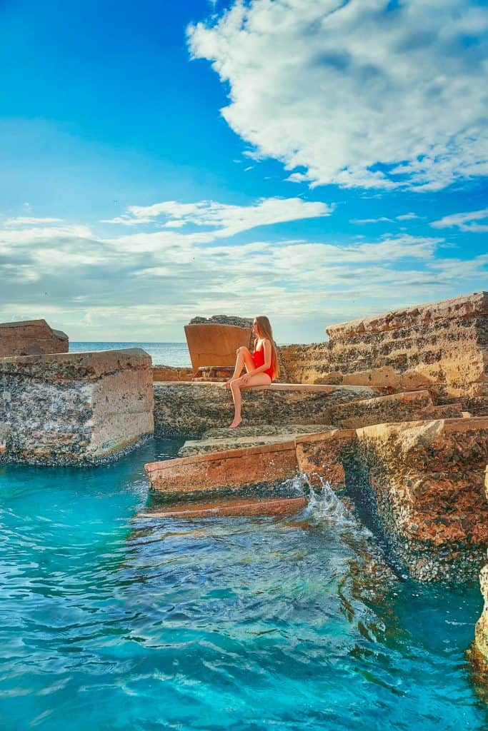Girl in red swimsuit sitting on the portion of Battery Bigelow fort that juts up out of the  turquoise water