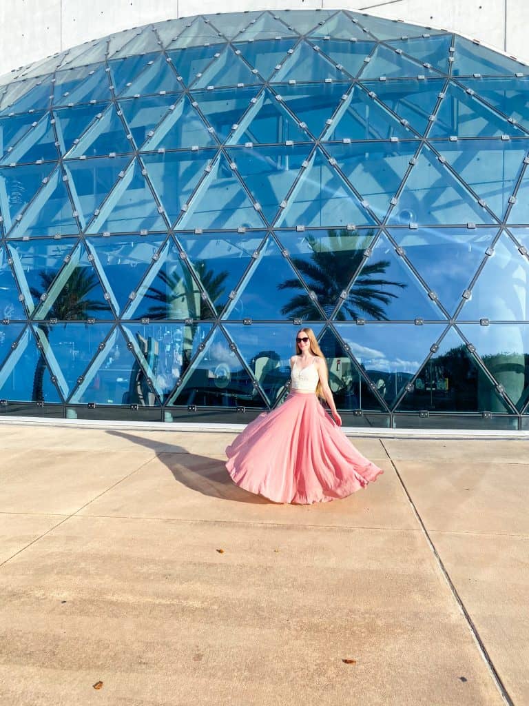 Girl in a pink long skirt poses in front of the glass dome of the Dali Museum in St. Pete