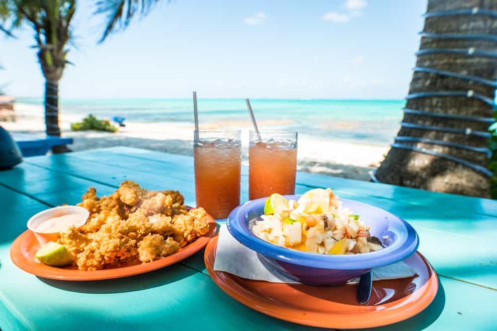 This restaurant in Key Largo serves Conch salad and fried seafood with two drinks on a teal picnic table overlooking the ocean with palm trees