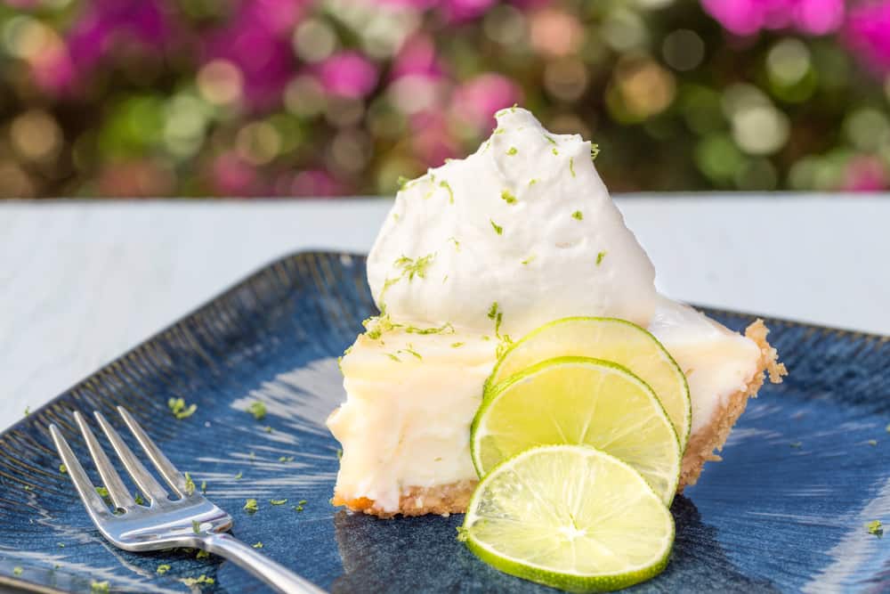 Slice of key lime pie with meringue and limes on a blue plate