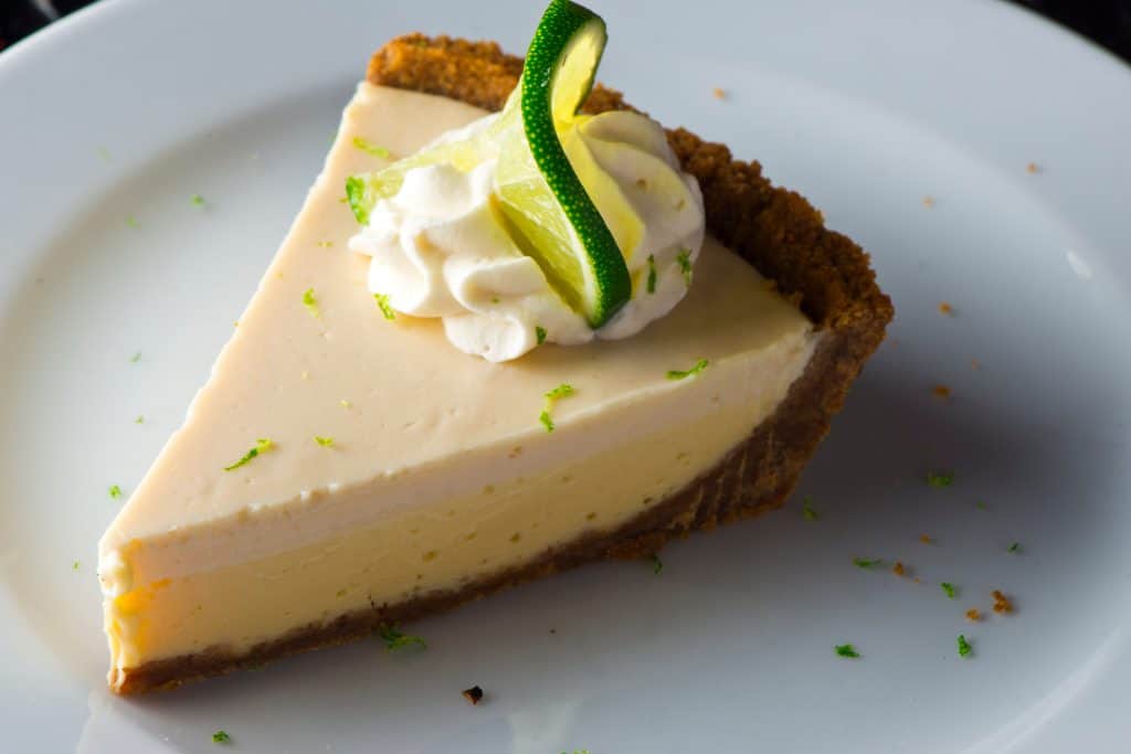 a delicious piece of Key Lime Pie rests on a plate with whipped cream.