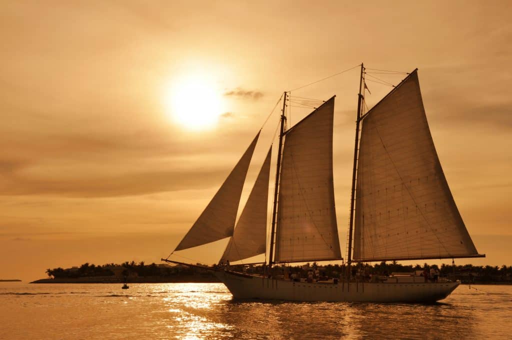 A catamaran sails through the sunset.