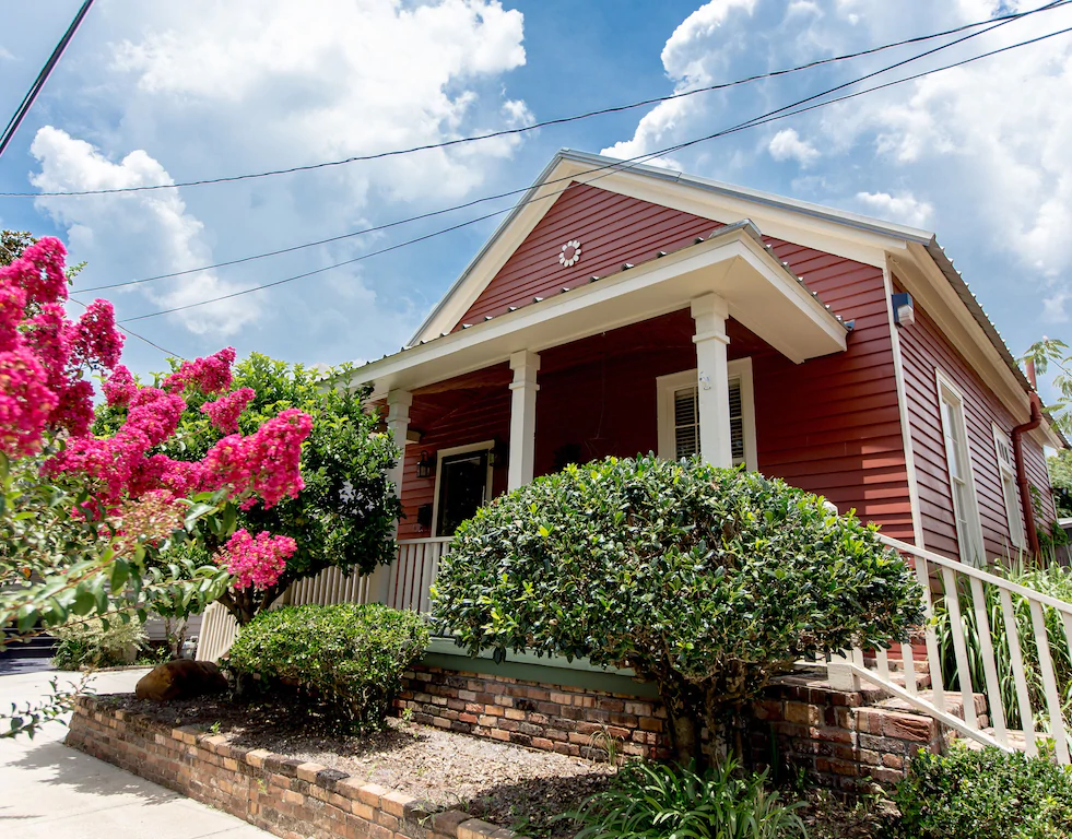 This beautiful little red cottage is one of the most quaint airbnbs in pensacola with a beautiful crepe myrtle plant just outside.