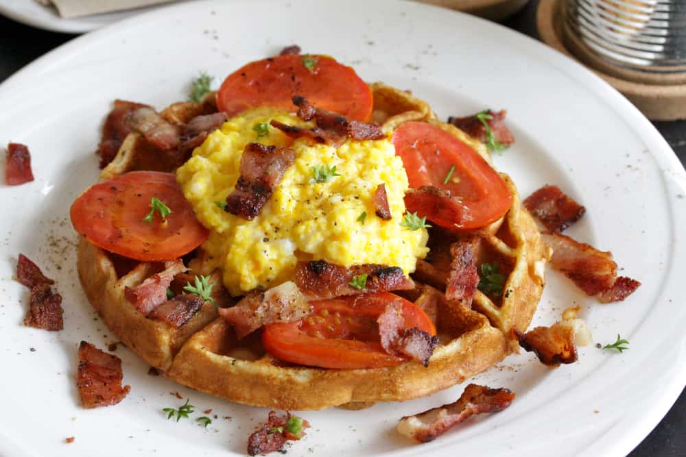 A waffle topped with bacon, tomatoes and eggs