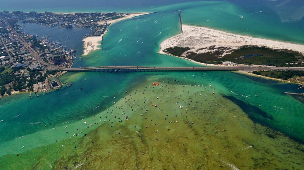 A drone image shows the sandbar of Crab Island adjacent to the Destin Harbor bridge.