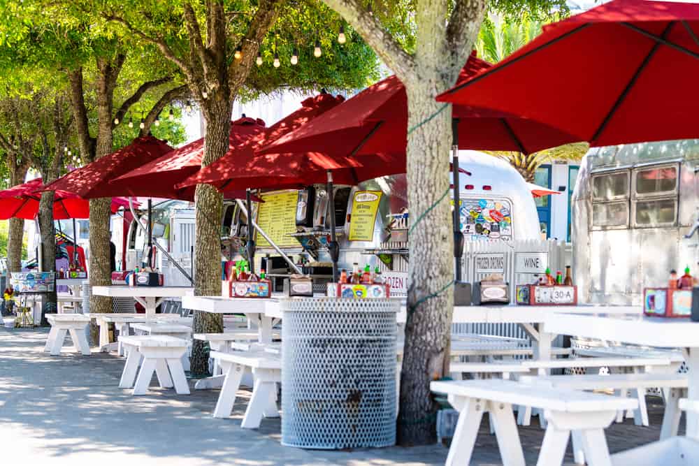 Picnic tables and umbrellas set up outside gourmet food trucks parked on Airstream Row, one of the best things to do in Seaside, Florida.