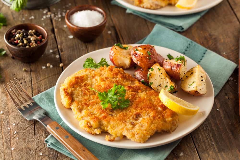 schnitzel on a plate with cut potatoes and herbs