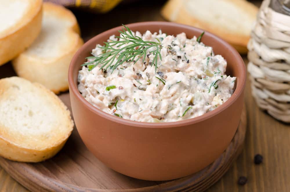brown bowl filled with smoked fish dip on a wooden plate with bread on it