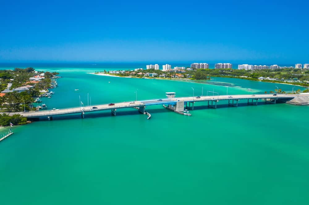 The incredible blue water of Siesta Key with a bridge over the water and buildings in the background.