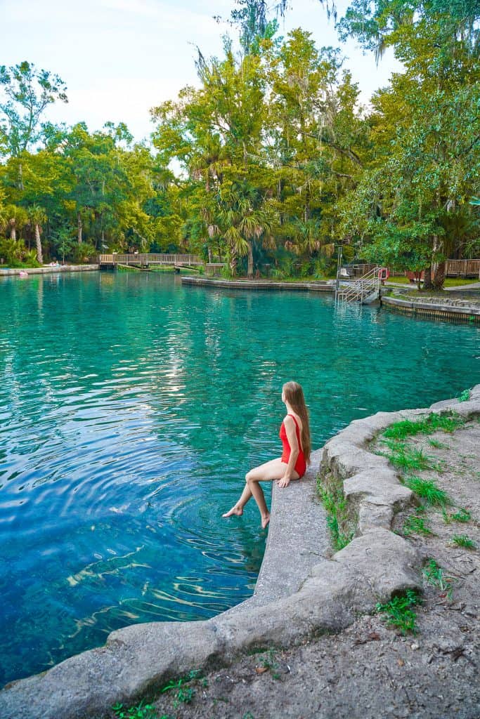 woman perched on stone border of blue waters of Wekiwa Spring