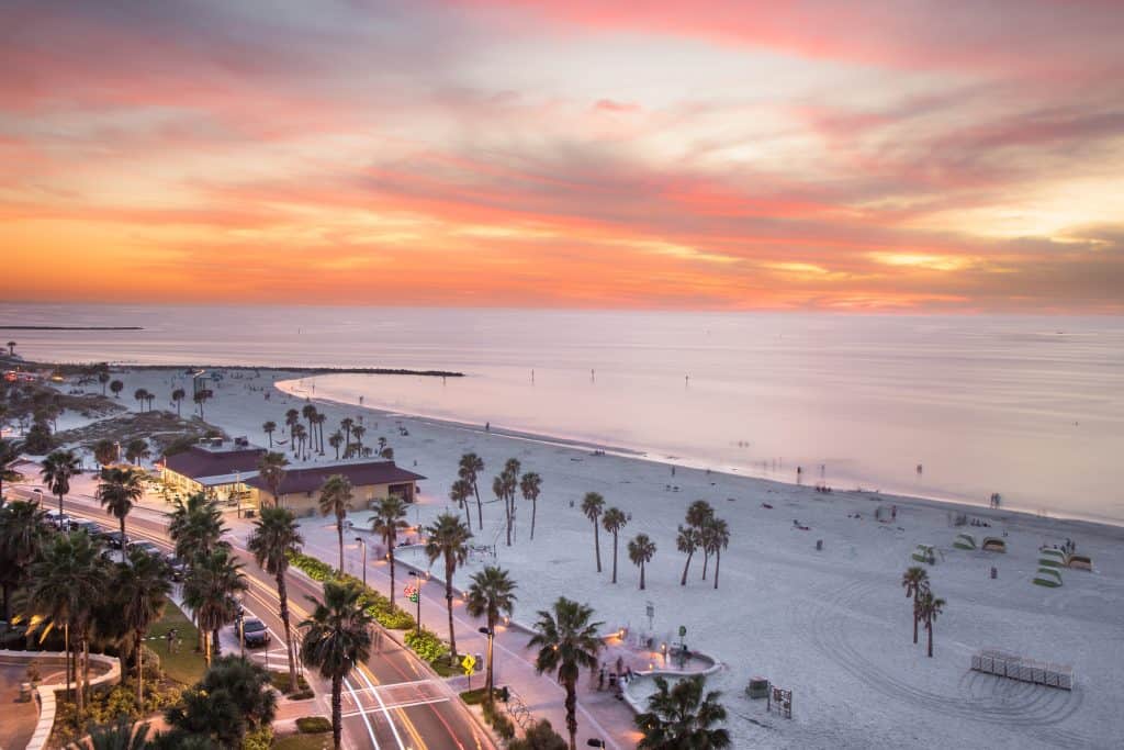 sunset on clearwater beach shot from above showing the road, palm tress and sunsetting over the ocean 