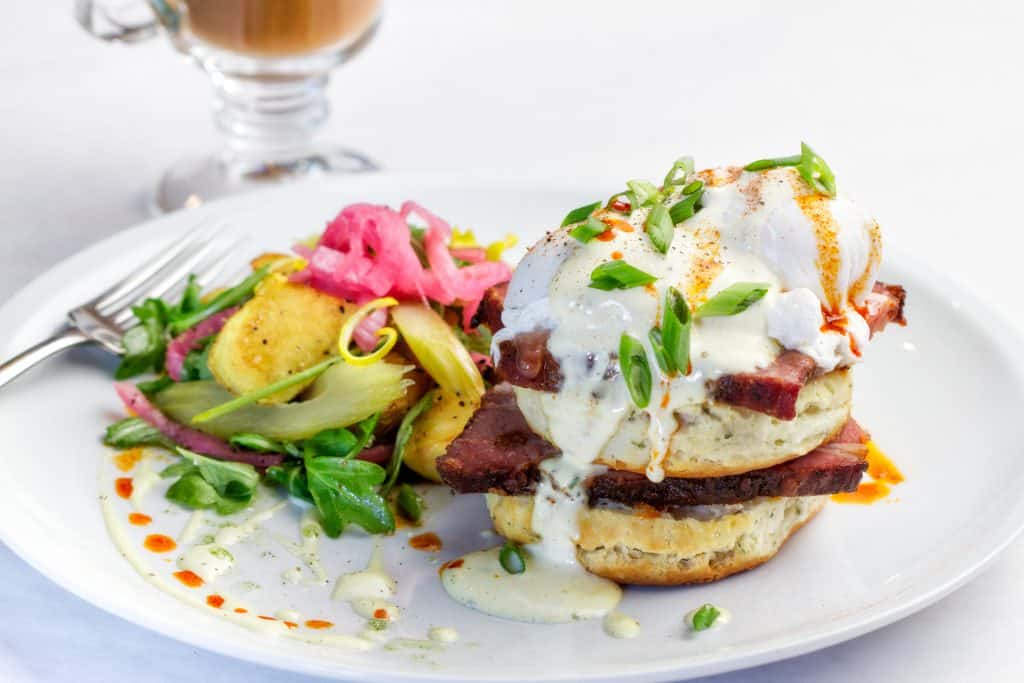 Eggs Benedict with steak, poached egg, and hollandaise sauce served with a colorful side salad.