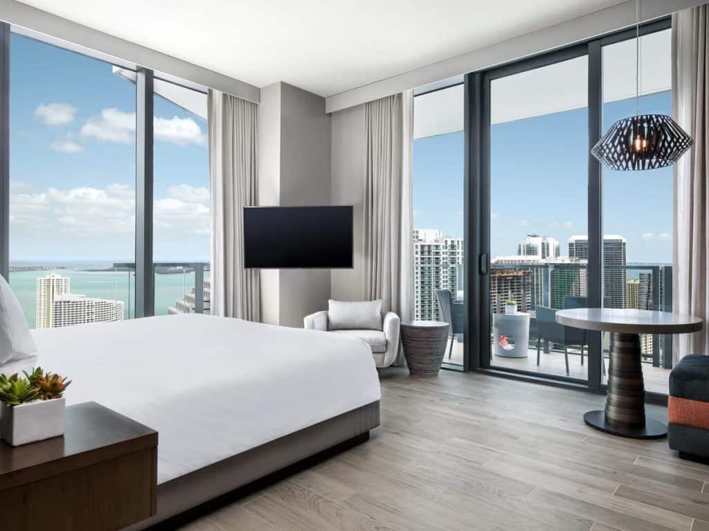 Modern hotel room with floor to ceiling windows and a balcony.