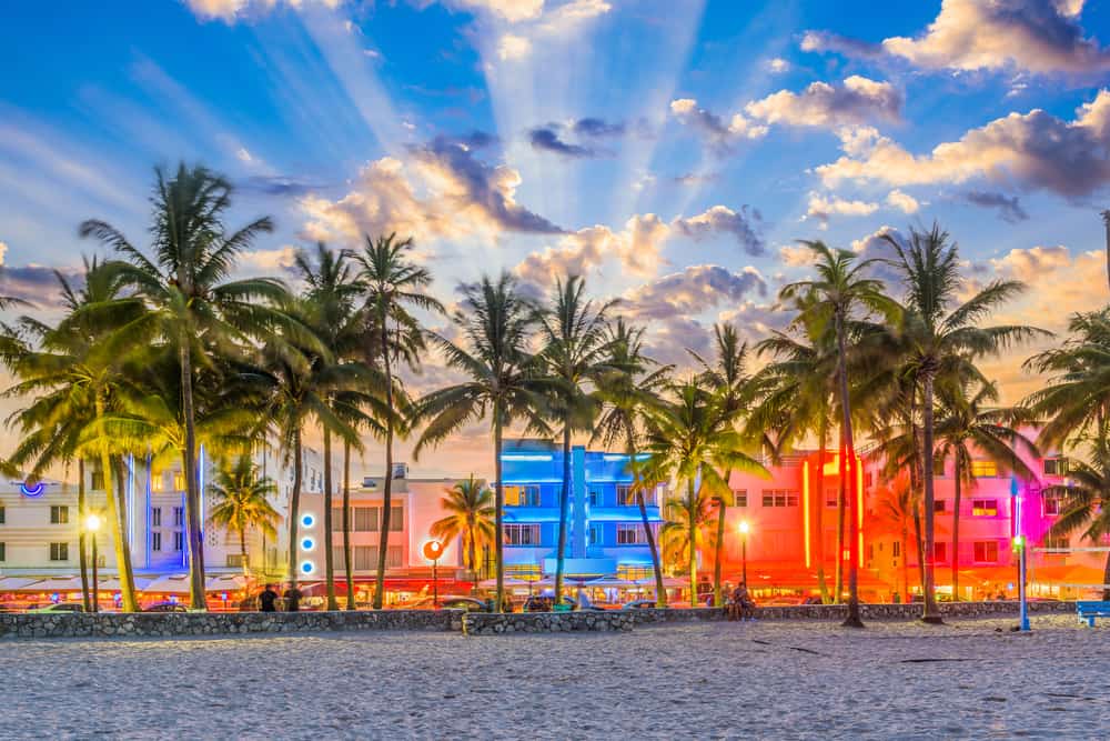 Looking from the beach towards a line of palm trees and colorful, Art Deco buildings at sunset.