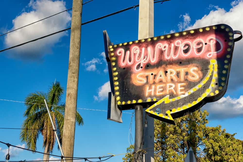 Old fashioned, spray painted sign that says "Wynwood Starts Here" with a yellow arrow.