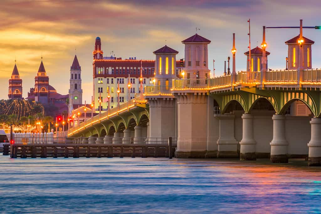 A large bridge crosses the water in St. Augustine, Florida with several building towers lit up at night during weekend getaways in Florida.