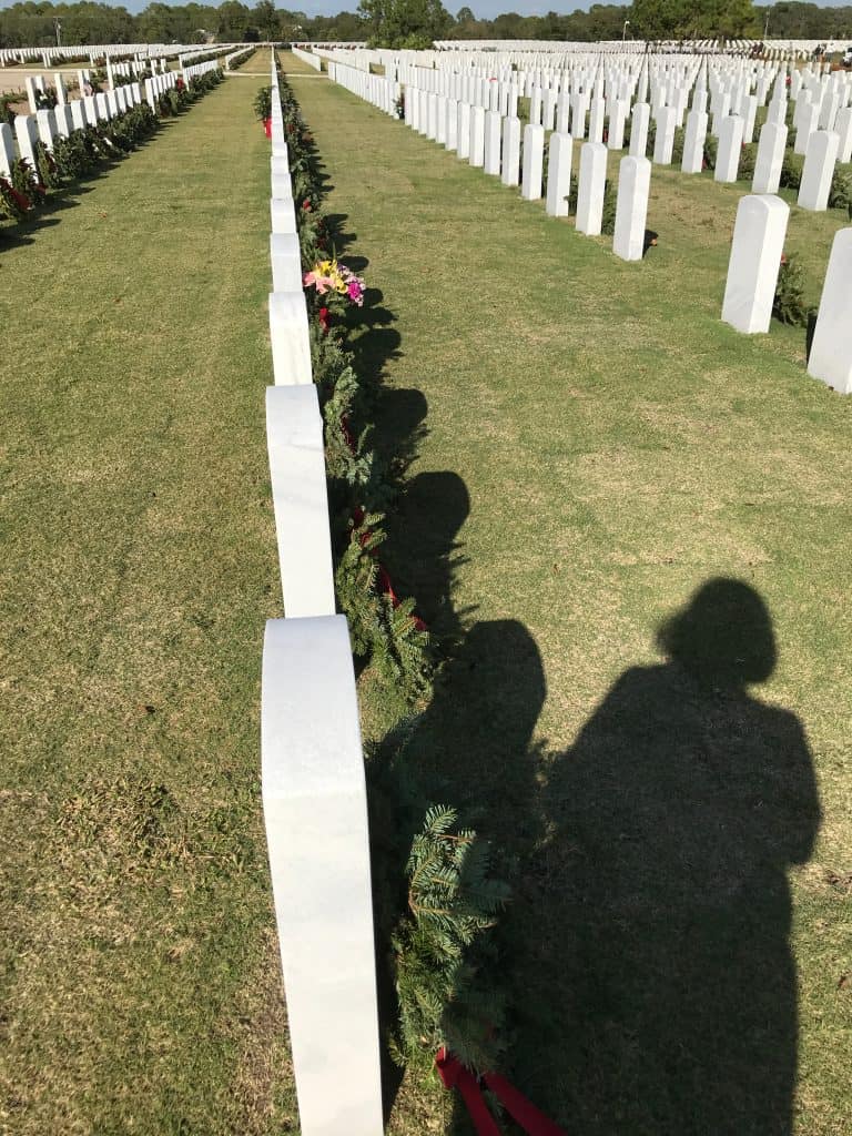 The shadows of mourners look on the lines of headstones in the Sarasota National Cemetery, adorned with wreaths. 