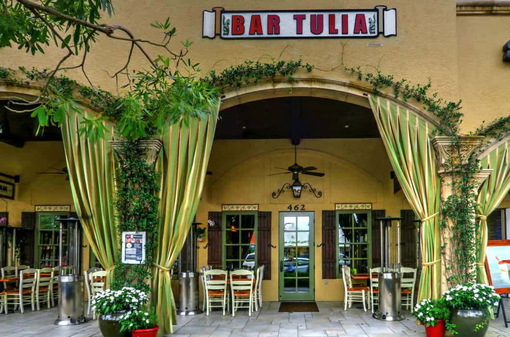 The yellow exterior with green curtains of Bar Tulia, one of the best restaurants in Naples, FL.