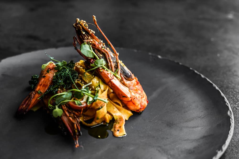 An elegant seafood dish with shrimp on a black plate.