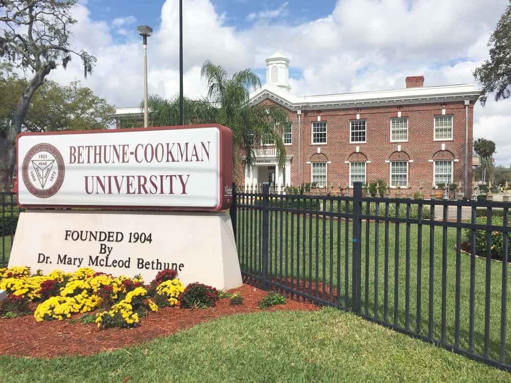 The sign for the Bethune-Cookman University with a brick building in the back.