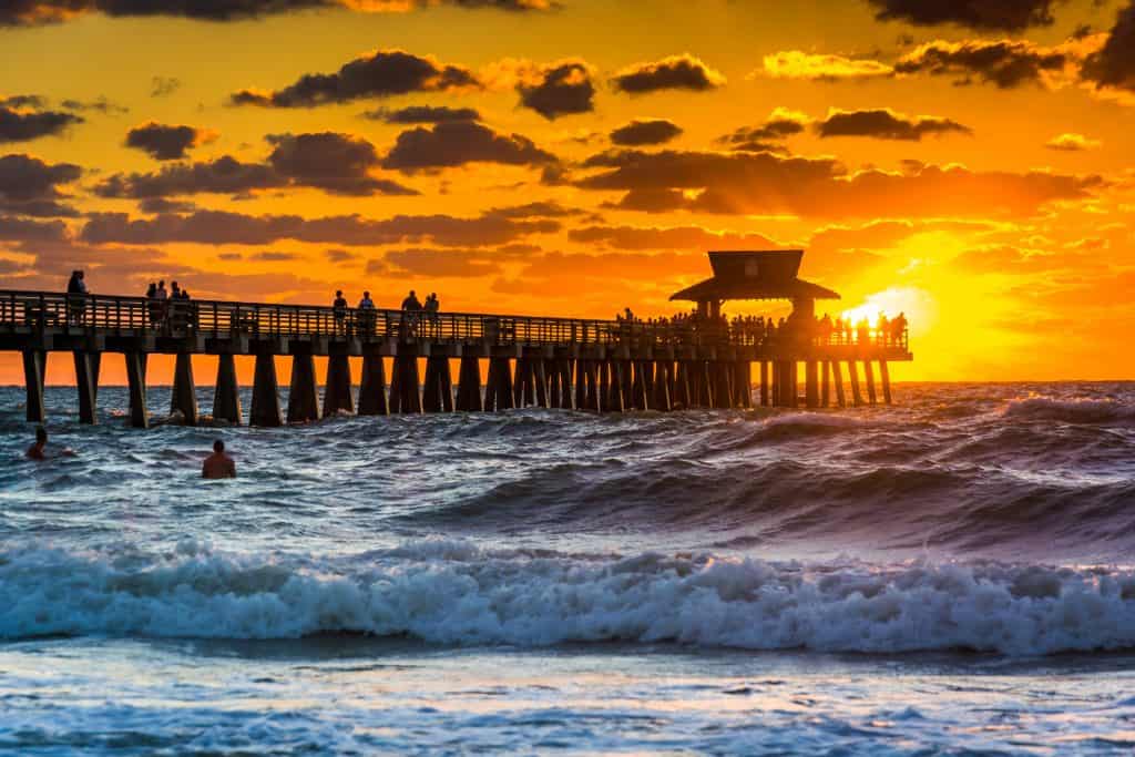 The sun sets on the Naples Pier as the waves crash onto the shore.