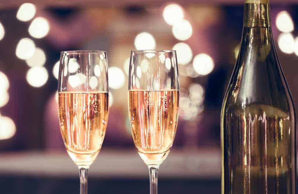 Photo of two champagne flutes next to a bottle of champagne.