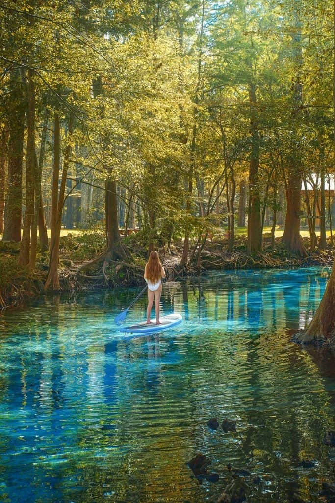 Woman with long hair stand up paddle boarding at Ginnie Springs during golden hour.