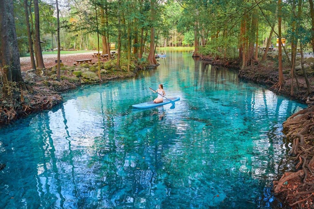 Woman sitting on a stand up paddle board in the bright blue spring water.