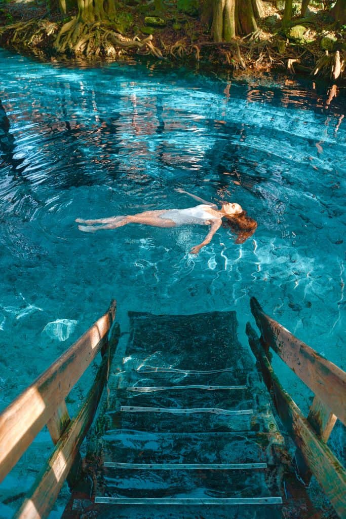 Stairs leading into blue, clear water with a woman floating on her back.