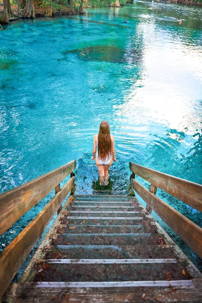 Woman with long hair walking down stairs into bright blue, clear water.